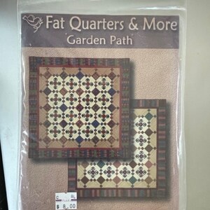 May include: A quilting pattern for a quilt called "Garden Path" designed by Diane deFreitas. The pattern is for a quilt with a geometric design in shades of red, blue, green, and white. The pattern is available for £8.00.
