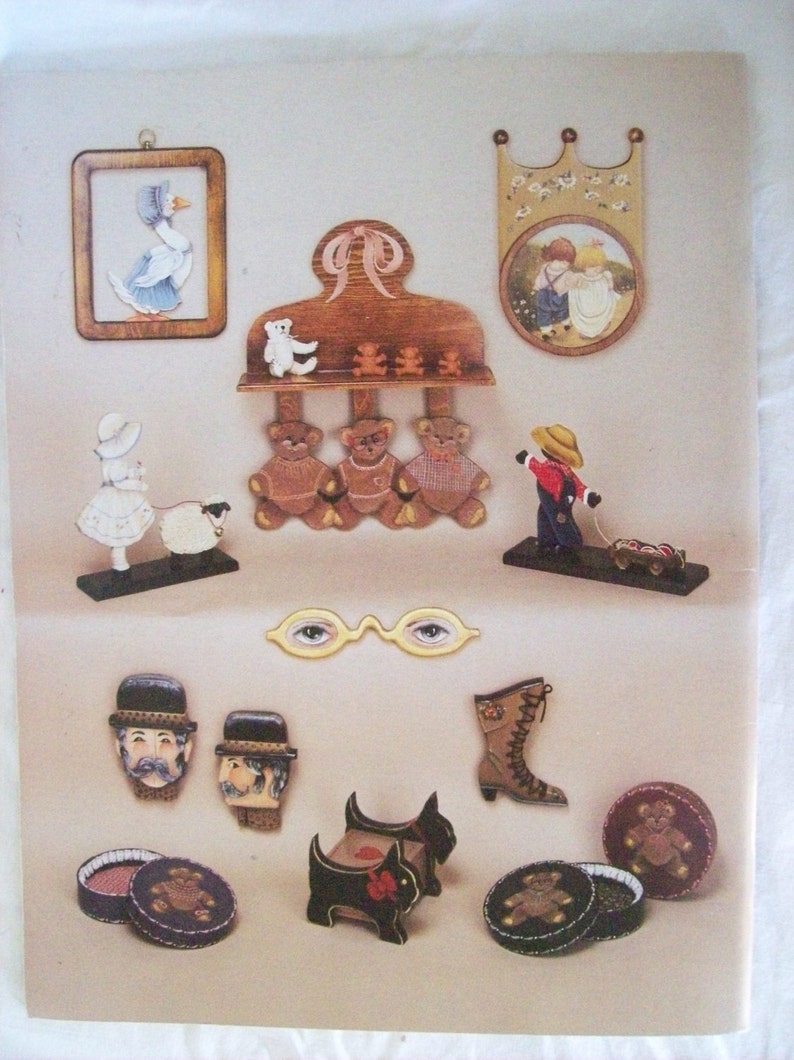 May include: A collection of wooden painted figurines, including a goose, a girl with a lamb, three teddy bears, a boy pulling a wagon, two men's faces, a boot, a dog, and a teddy bear in a round box.
