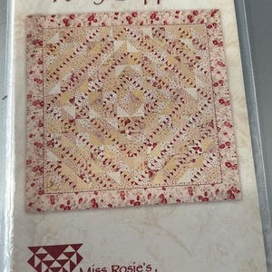 May include: A quilt pattern titled "Ruby Slippers" by Miss Rosie's Quilt Co. The pattern features a square design with a central geometric pattern in cream, red, and white, framed by a floral border. The number 26 is visible.