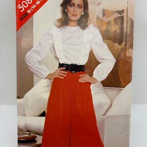 May include: A vintage sewing pattern package with the text "See & Sew 5084 SIZE B (14-16-18)". The package features a woman wearing a white blouse with ruffles, a black belt, and rust-colored culottes. The background is a neutral color.