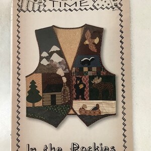 May include: A brown and tan quilted vest with a patchwork design featuring a cabin, mountains, a bear, a moose, a bird, and a canoe. The vest is surrounded by a black border with the text "Scraps of Time" and "In the Rockies".