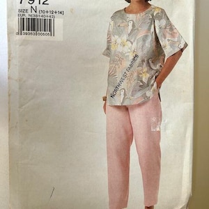 May include: A vintage sewing pattern featuring a woman wearing a top and pants. The top has a floral and bird print with the text "NORTHWEST FABRICS". The pants are a light pink color. The pattern is labeled "AVER 7912".