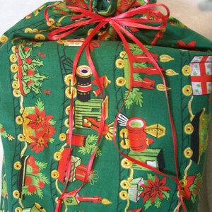 Puede incluir: Una bolsa de regalo de tela verde con una cinta roja y un patrón de tren de Navidad. La bolsa está llena de regalos y está lista para ser entregada.