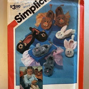 Könnte beinhalten: Simplicity Schnittmuster Nummer 6231 zum Nähen von Tierpantoffeln für Kinder. Das Schnittmuster zeigt fünf verschiedene Tierpantoffeln: einen Löwen, einen Bären, ein Kaninchen, eine Katze und eine Maus. Das Schnittmuster enthält auch ein Foto eines Kindes, das ein Paar Hasenpantoffeln trägt.