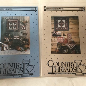 Pode incluir: Dois padrões de ponto cruz da Country Threads, um intitulado "Broken Hearts" #112 e o outro "Log Cabin Hearts" #103. Ambos os padrões apresentam um design rústico de estilo campestre com corações e motivos de cabana de madeira.