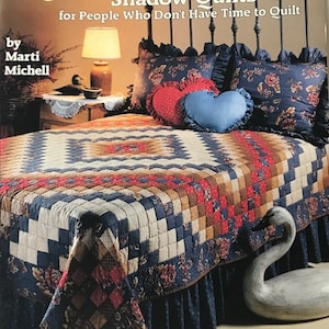 Peut inclure: Un livre intitulé "Strip, Trip and Shadow Quilts for People Who Don't Have Time to Quilt" par Marti Michell. La couverture du livre présente une courtepointe sur un lit avec une figurine de cygne au pied du lit. Le livre fait partie d'une série intitulée "Quilting for People Who Don't Have Time to Quilt".