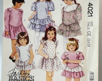 May include: A sewing pattern for children's dresses. The pattern includes five different dress styles, all with a variety of floral prints and colors. The pattern is for sizes 3, 4, and 5. The pattern is called "Fashion Basics for Kids" and is from McCall's.
