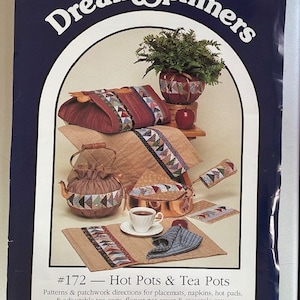 May include: A book cover for a quilting pattern book titled "Dream Spinners #172 - Hot Pots & Tea Pots". The cover features a variety of quilted items, including a tea cozy, a casserole cover, and a flower pot cover. The book is by Nancy J. Smith and Lynda S. Milligan and was published in 1991.