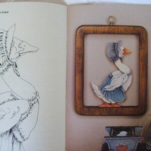 May include: A black and white line drawing of a goose wearing a bonnet and dress. The goose is in a frame with a painted goose wearing a bonnet and dress. The painted goose is in a blue dress with white accents. The goose is holding a string attached to a painted rabbit wearing a blue dress with white accents.