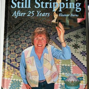 May include: A book cover titled "Still Stripping After 25 Years" by Eleanor Burns. The cover features a woman wearing a patchwork vest, smiling, and holding up her hand. The background is a colorful quilt pattern. The book is from "Quilt in a Day".