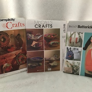 May include: Three craft pattern envelopes from Simplicity, McCall's, and Butterick. The Simplicity envelope features a wreath and other holiday decorations. The McCall's envelope shows bowls. The Butterick envelope shows bags and a woman wearing a visor.