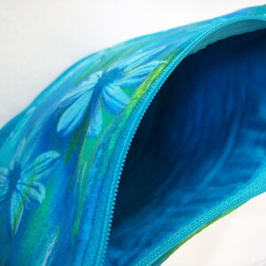 May include: A blue zippered pouch with a floral print featuring blue and green flowers. The pouch is open, revealing a bright blue lining.