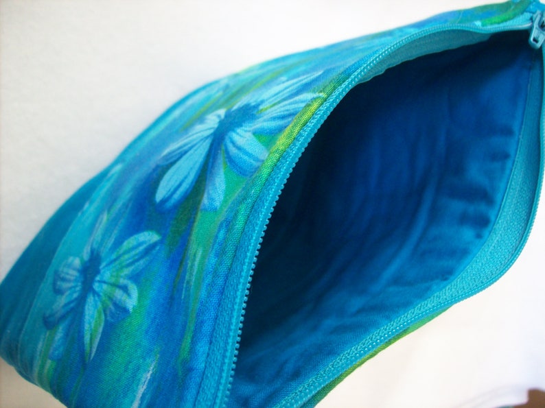 May include: A blue zippered pouch with a floral print featuring blue and green flowers. The pouch is open, revealing a bright blue lining.