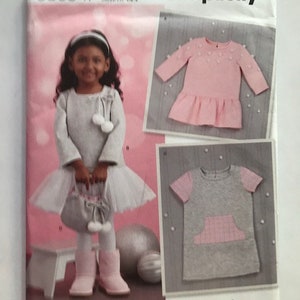 May include: Simplicity sewing pattern number 8805 for girls' dresses. The pattern includes two dress styles: a grey dress with a pink pocket and a pink dress with white pearl embellishments. The pattern is for sizes 12-18 months, 18-24 months, 2T, 3T, 4T.