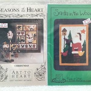 May include: Two cross-stitch patterns for Christmas. The first pattern is called "Seasons of the Heart" and features a Christmas tree with decorations. The second pattern is called "Santa in the Woods" and features Santa Claus standing in a snowy forest.