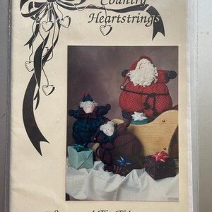 May include: A craft pattern for making a 16-inch Santa and a 10-inch elf doll. The pattern is titled "Country Heartstrings" and features a photo of the finished dolls.