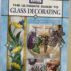 Peut inclure: Livre intitulé "The Ultimate Guide to Glass Decorating" par Jan Cumber. La couverture présente un bocal en verre décoré de fleurs violettes et de libellules. Guide complet pour créer des projets d'art sur verre.