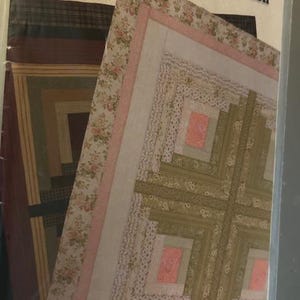 Puede incluir: Un patrón de colcha con un diseño de cabaña de troncos en un esquema de color marrón, verde y rosa. El patrón se llama "His & Hers #QY24".