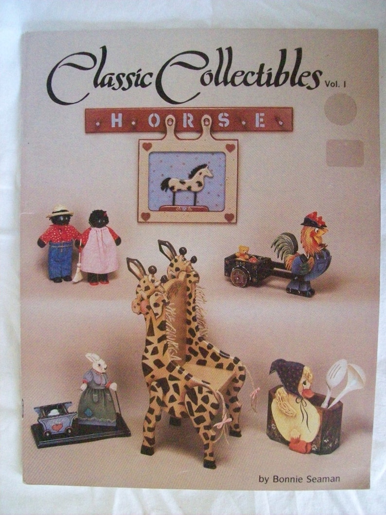 May include: A book titled "Classic Collectibles Vol. I" featuring painted wooden figurines of a horse, giraffe, rooster, bunny, and duck. The book includes instructions for painting these figurines.