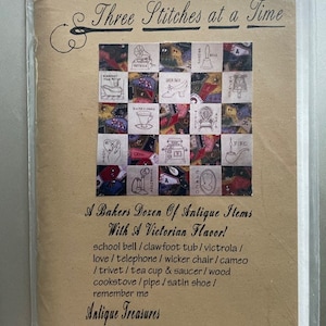 May include: A brown paper booklet with the title "Three Stitches at a Time" and a picture of a sampler with 16 squares, each containing a different antique item. The text below the image reads "A Baker's Dozen of Antique Items With A Victorian Flavor!" and lists the items included in the sampler. The booklet is for sale for $10.00.