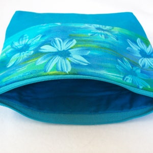 May include: A turquoise zippered pouch with a floral print featuring blue flowers on a turquoise background.