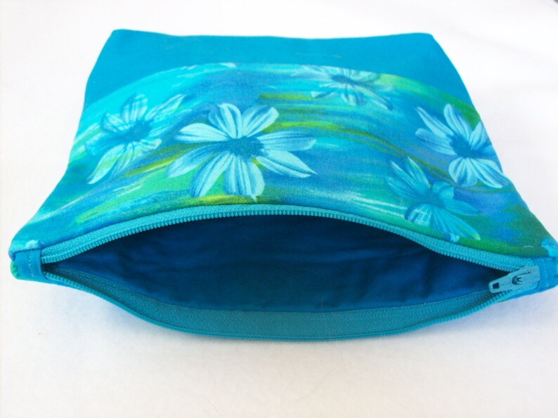 May include: A turquoise zippered pouch with a floral print featuring blue flowers on a turquoise background.