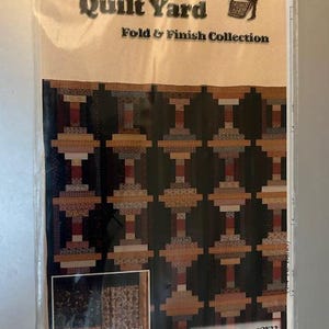 Puede incluir: Un patrón de acolchado para una colcha llamada "Courthouse Steps" de la colección The Quilt Yard Fold & Finish. El patrón presenta un diseño geométrico con telas marrones, tostadas y rojas.
