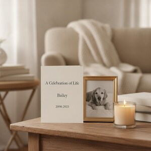 以下が含まれることがあります： 「A Celebration of Life」「Bailey」「2008-2023」と書かれたクリーム色のメモリアルカード。その隣には、犬の白黒写真が入った金色のフォトフレームと、透明なガラスホルダーに入った火のついた白いキャンドルが置かれています。