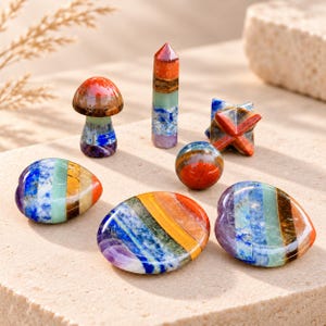 May include: A collection of seven polished multi-colored stones featuring horizontal bands of red, orange, yellow, green, blue, and purple. The set includes a mushroom shape, a tower, a star, a sphere, and three heart-shaped stones.