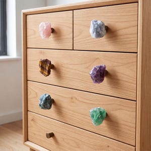 May include: A light-toned wooden dresser featuring six drawers, five of which are fitted with raw, irregular gemstone knobs in pink, blue, brown, purple, teal, and green, while the bottom drawer has a simple round metal knob.