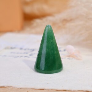 May include: A smooth, polished green stone ring holder shaped like a cone. The object features a solid, vibrant green color with subtle natural variations in the stone texture, standing upright with a wide circular base and a rounded top point.