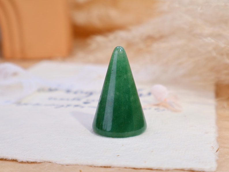 May include: A smooth, polished green stone ring holder shaped like a cone. The object features a solid, vibrant green color with subtle natural variations in the stone texture, standing upright with a wide circular base and a rounded top point.