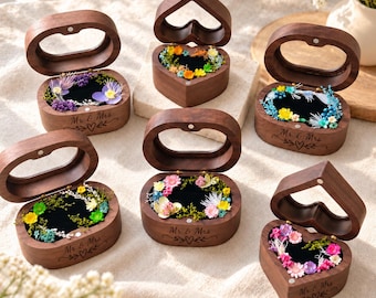 May include: Six dark wood ring boxes with hinged lids and glass windows. Each box features a black velvet interior filled with colorful dried flowers and the engraved text Mr. & Mrs. with a heart icon on the front exterior.