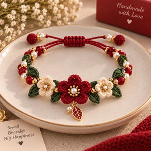 May include: A red cord bracelet featuring a central dark red woven flower, two cream-colored woven flowers, and green woven leaves. The design includes small white pearls, gold beads, and a gold leaf charm. Text on cards reads "Handmade with Love" and "Small Bracelet Big Happiness."