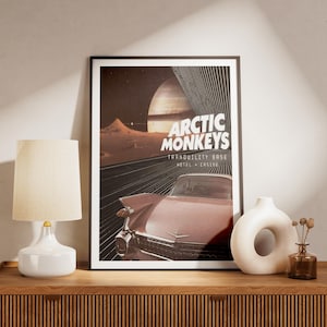 May include: A framed rectangular poster featuring a vintage pink car driving on a dark road toward a large planet and lunar landscape. The text reads Arctic Monkeys and Tranquility Base Hotel + Casino in white lettering against a dark background.