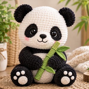 Puede incluir: Un peluche de panda tejido a ganchillo con hilo blanco y negro, con grandes ojos oscuros, mejillas rosadas y una nariz bordada. El panda sostiene un tallo de bambú tejido en verde con hojas pequeñas en sus brazos y tiene almohadillas blancas.