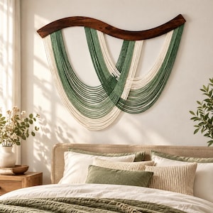 May include: A wall hanging featuring a curved, dark brown wooden top piece with multiple strands of forest green and cream-colored cord draped in overlapping, U-shaped patterns, creating a layered, symmetrical design across the wall.