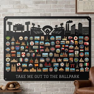 May include: A black metal wall art piece featuring a baseball stadium silhouette at the top and numerous colorful travel-themed circular and rectangular icons below. The text "TAKE ME OUT TO THE BALLPARK" is printed in white at the bottom.