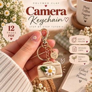Op de afbeelding: Een camera-sleutelhanger van polymeerklei met een wit madeliefje met een geel hartje aan de voorzijde. De sleutelhanger is voorzien van een goudkleurige metalen karabijnhaak, een sleutelring en een klein rond bedeltje met de tekst Good Things.