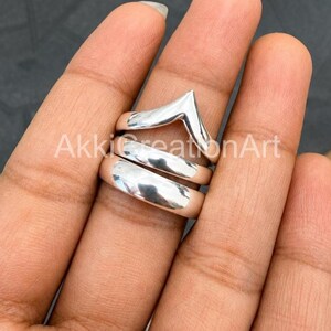 May include: A set of three polished silver-toned rings stacked together. The top ring features a V-shaped chevron design, while the middle and bottom rings are smooth, plain bands with a reflective metallic finish and a rounded profile.