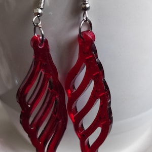 Könnte beinhalten: Ein Paar Ohrhänger mit durchscheinenden roten Acryl-Anhängern in einem ausgeschnittenen, wirbelnden blattartigen Muster. Die Anhänger sind an silberfarbenen Metall-Ohrhaken befestigt und bilden ein leichtes, leuchtendes Accessoire.