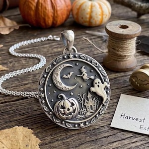 Puede incluir: Un colgante redondo de plata con un diseño en relieve que muestra una luna creciente, una bruja volando en una escoba, un fantasma, una calabaza y una casa encantada. El borde está decorado con estrellas y hojas.