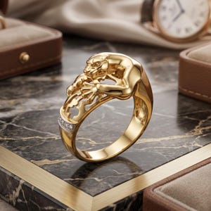 Könnte beinhalten: Ein goldener Ring mit einer skulptierten Pantherfigur, die auf dem Ringband ruht. Der Panther ist in einer kauernden Position dargestellt, wobei der Kopf nach vorne gerichtet ist. Ein kleiner Teil des Bandes ist mit einer Reihe kleiner, klarer Steine besetzt.