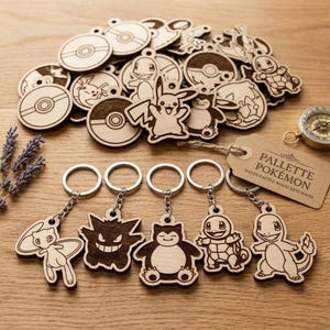 May include: A collection of light-colored wooden keychains featuring laser-engraved Pokemon characters and Poke Balls. Five keychains are displayed in the foreground with metal rings, while a pile of additional wooden pieces sits behind them.