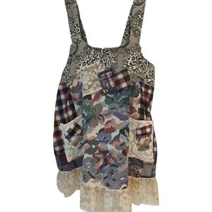 May include: A sleeveless apron dress featuring a patchwork design of various fabrics including plaid, floral, leopard print, and lace. The garment has two front pockets, wide shoulder straps, and a cream-colored lace trim along the bottom hem.