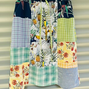 May include: A patchwork skirt with a variety of patterns, including tropical leaves, pineapples, toucans, and floral designs. The skirt features a mix of blue, green, yellow, and white fabrics, creating a vibrant and eclectic look. The waistband is dark blue with a drawstring.