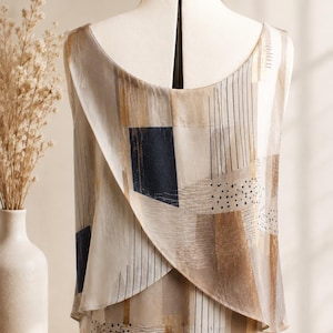 Peut inclure: Un haut sans manches présentant un design arrière superposé et croisé sur une base beige. Le tissu est orné d'un motif géométrique composé de rectangles bleu marine foncé, de lignes noires verticales, de touches dorées et de petits points noirs.