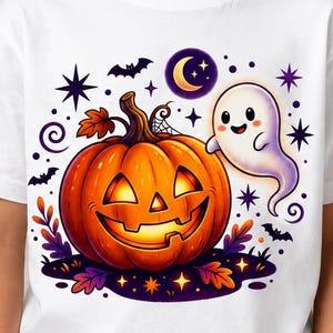 May include: A white short-sleeved t-shirt featuring a colourful graphic of a smiling jack-o'-lantern pumpkin, a small white ghost, a crescent moon, stars, and bats. The design includes purple and orange accents with autumn leaves at the base.