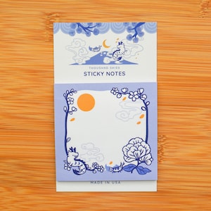 May include: A pack of sticky notes with a blue and white design featuring a dragon and clouds. The text "Thousand Skies Sticky Notes" is printed on the front of the pack. The notes are made in the USA.