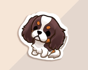 Może przedstawiać: Naklejka z kreskówkową ilustracją brązowo-białego Cavalier King Charles Spaniela z brązowymi oczami i czarnym nosem. Pies patrzy w dół i ma białą klatkę piersiową oraz brązowo-pomarańczową plamę na głowie. Naklejka zawiera napis "THOUSANDSKIES" po prawej stronie.